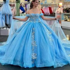 Transform your quinceanera into a magical fairytale with this Sky Blue Ball-Gown Dress. This dress features a dreamy off-the-shoulder neckline that exudes timeless elegance. The ball gown silhouette and flowing chapel train create a grand and majestic presence. It is crafted from delicate tulle fabric and is adorned with intricate appliques and shimmering sequins, adding a touch of sparkle to every step. The highlight of this dress is the stunning matching cape, which drapes gracefully for an et Blue Ball Gown With Fitted Bodice For Pageant, Blue Ball Gown With Fitted Bodice For Pageants, Blue Princess Style Floor-length Gown, Light Blue Princess Ball Gown, Light Blue Princess Style Ball Gown, Princess Style Light Blue Ball Gown, Light Blue Tulle Gown For Quinceanera, Princess Style Light Blue Prom Gown, Blue Tulle Floor-length Ball Gown