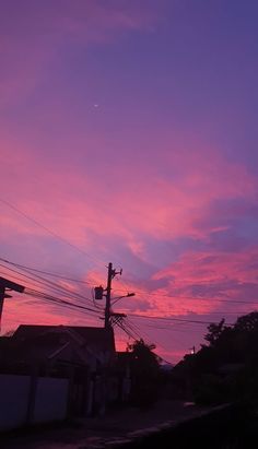 the sky is pink and purple as the sun sets in the distance behind some houses