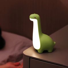 a green dinosaur lamp sitting on top of a nightstand next to a person's hand