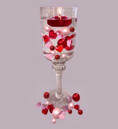 a wine glass filled with lots of pink and red heart shaped confetti next to a lit candle