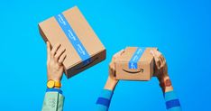 two hands holding up boxes with an amazon logo on them, against a blue sky