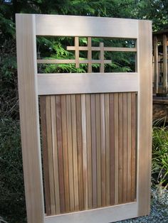 a wooden gate is shown in front of some bushes and trees, with the top part of it made out of wood slats