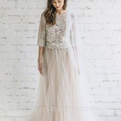 a woman standing in front of a white brick wall wearing a dress with long sleeves