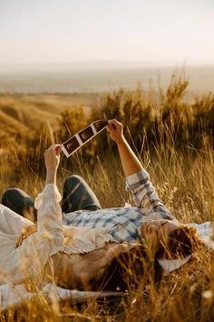 a man laying in the grass with his cell phone up to his face and reading it