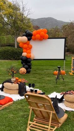 an outdoor movie party with balloons and pumpkins on the grass in front of a large screen