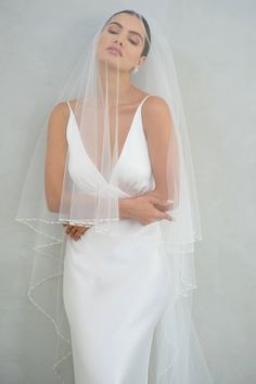 a woman wearing a white wedding dress with a veil on her head and one hand under her chin