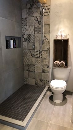 a white toilet sitting in a bathroom next to a walk in shower and tiled walls