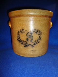 a brown pot with a wreath on the side and two hands in the middle is sitting on a blue surface