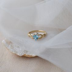 Delicate and symbolic Claddagh ring is made out of 14k solid gold and set with blue heart topaz and diamond It would make a perfect choice for the engagement or as a push gift. Ring can be made in white, rose or yellow 14k gold. Highly polished. If you want to customise this product or set it with another stones - please write to us. ❤ Hand Made with love in our studio in Prague ❤ Stone details Topaz Shape: Heart Dimensions: 5.7 mm Color: Blue Origin: Natural Diamond Amount: 1 Shape: Round Color Topaz Birthstone Promise Ring Fine Jewelry, Topaz Birthstone Promise Ring In Fine Jewelry Style, Fine Jewelry Topaz Birthstone Promise Ring, 14k Gold Heart Ring With Birthstone For Promise, Heart Cut Topaz Ring For Promise, Heart Cut Topaz Gemstone Ring For Promise, Dainty Topaz Ring With Birthstone, Heart Cut Topaz Promise Ring, Promise Yellow Gold Topaz Birthstone Ring