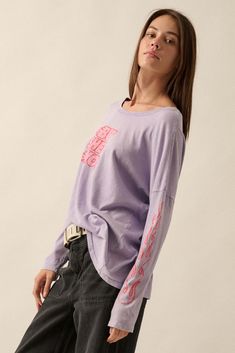 Mineral washed graphic t-shirt. Vintage-style "But She's Hot" text print with flame graphics. Long sleeves with flame print. Dropped shoulder. Round neckline. Center-back seam. Oversized fit. 100% Cotton. Imported top designed and printed in LA. Model wears size S. Purple Letter Print Tops For Streetwear, Purple Long Sleeve Top With Graphic Print, Casual Purple Top With Graphic Print, Acid Wash Oversized Top With Text Print, Oversized Acid Wash Top With Text Print, Spring Lavender Letter Print Top, Purple Graphic Tee Tops For Streetwear, Relaxed Fit Lavender Graphic Tee, Oversized Purple Top With Text Print