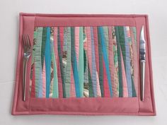 a pink placemat with colorful strips of fabric and silverware sitting on top of it