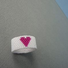 a white and pink beaded bracelet with a red heart on it's side