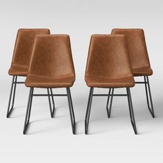 three brown leather chairs sitting next to each other on top of a white floor with black metal legs