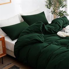 a bed with green sheets and pillows on top of it next to a potted plant