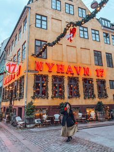 a woman standing in front of a building with christmas decorations on the windows and lights