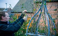 a man is pruning plants in front of a brick building with vines growing on it