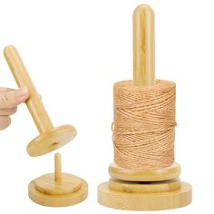 a hand holding a spool of twine next to a wooden spinning wheel