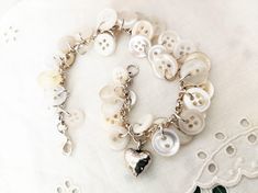 a white bracelet with lots of buttons and charms on it's chain, sitting on a lace doily