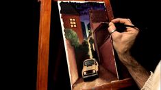 a man is drawing on an easel with a car in the street and buildings behind him