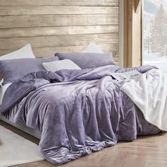 a bed with purple comforter and pillows in front of a wooden headboard that has snow on it