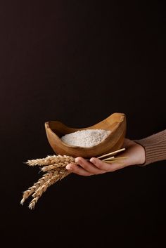 a person holding a wooden bowl with grain in it