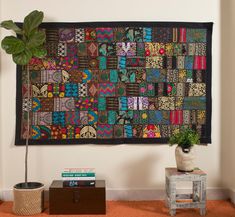 a patchwork wall hanging on the wall next to a small table with a potted plant