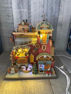 a toy house with lights and decorations on the top floor, in front of a wooden paneled wall