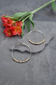 Our gold and silver tone hoop earrings with a round gold tone bead near where the earring hooks, showcases 11 gold and silver tone beads in 2 different styles in a simple design. The earrings hang from a hooked wire for easy wear. Every pair of these beautiful earrings has been handcrafted by at-risk and rescued women in Thailand. Dimensions: 2" diameter. Elegant Metal Beaded Hoop Earrings, Formal Gold-plated Hoop Earrings With Ear Wire, Silver Gold-plated Hoop Earrings With Ear Wire, Gold-tone Metal Hoop Earrings With Ear Wire, Nickel-free Small Hoop Metal Beaded Earrings, Gold Bubbles, Pearl Shop, Coin Earrings, Coin Pearls