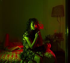 a woman sitting on top of a bed in a dark room with red light coming from her