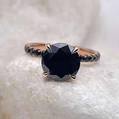 a black diamond ring sitting on top of a white rock with the stone in it's center