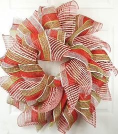 a red and green mesh wreath hanging on the front door with a white wall behind it