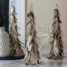 three fake trees are sitting next to a white vase and candle holder on the floor