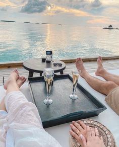 two people sitting at a table with champagne glasses on it and the ocean in the background