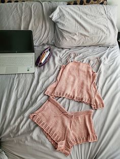 two pieces of clothing on a bed next to a laptop