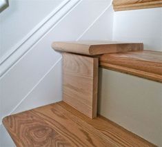 the corner of a wooden stair case in a room with white walls and wood flooring