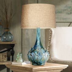 a blue vase sitting on top of a wooden table next to a white chair and lamp