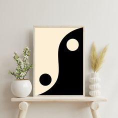 a black and white abstract art print on a shelf next to a vase with flowers