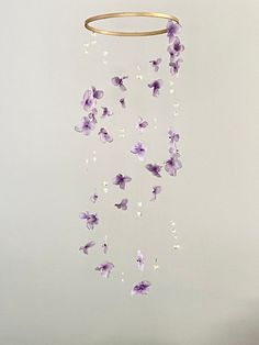 a mobile with purple flowers hanging from it's side on a table in front of a white wall