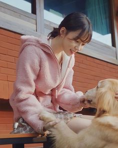 a woman in pink jacket petting a dog on the side of a brick building