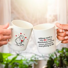 two people holding coffee mugs with the words sitting next to each other on them