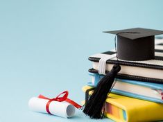 a graduation cap sitting on top of books next to a rolled up book with a red ribbon