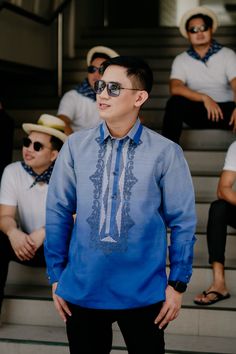 a man wearing sunglasses and a blue shirt standing in front of some stairs with other men