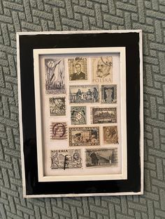 a black and white frame with stamps in it on a gray wall next to a carpet