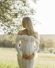 a pregnant woman standing in the grass with her hands on her hips and looking off to the side