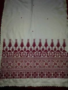 a red and white table cloth with an intricate design on the border, sitting on top of a bed