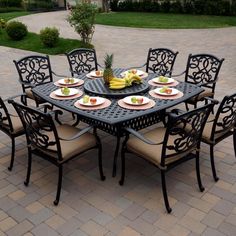 an outdoor dining table with six chairs and plates on it, in the middle of a brick patio