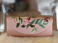 a pink purse with flowers and leaves painted on the front is sitting on a furnishing