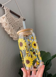 a person holding up a glass with sunflowers painted on it