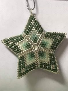 a green and white beaded star ornament hanging from a silver plated chain