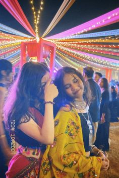 two young women standing next to each other in front of a tent covered with lights